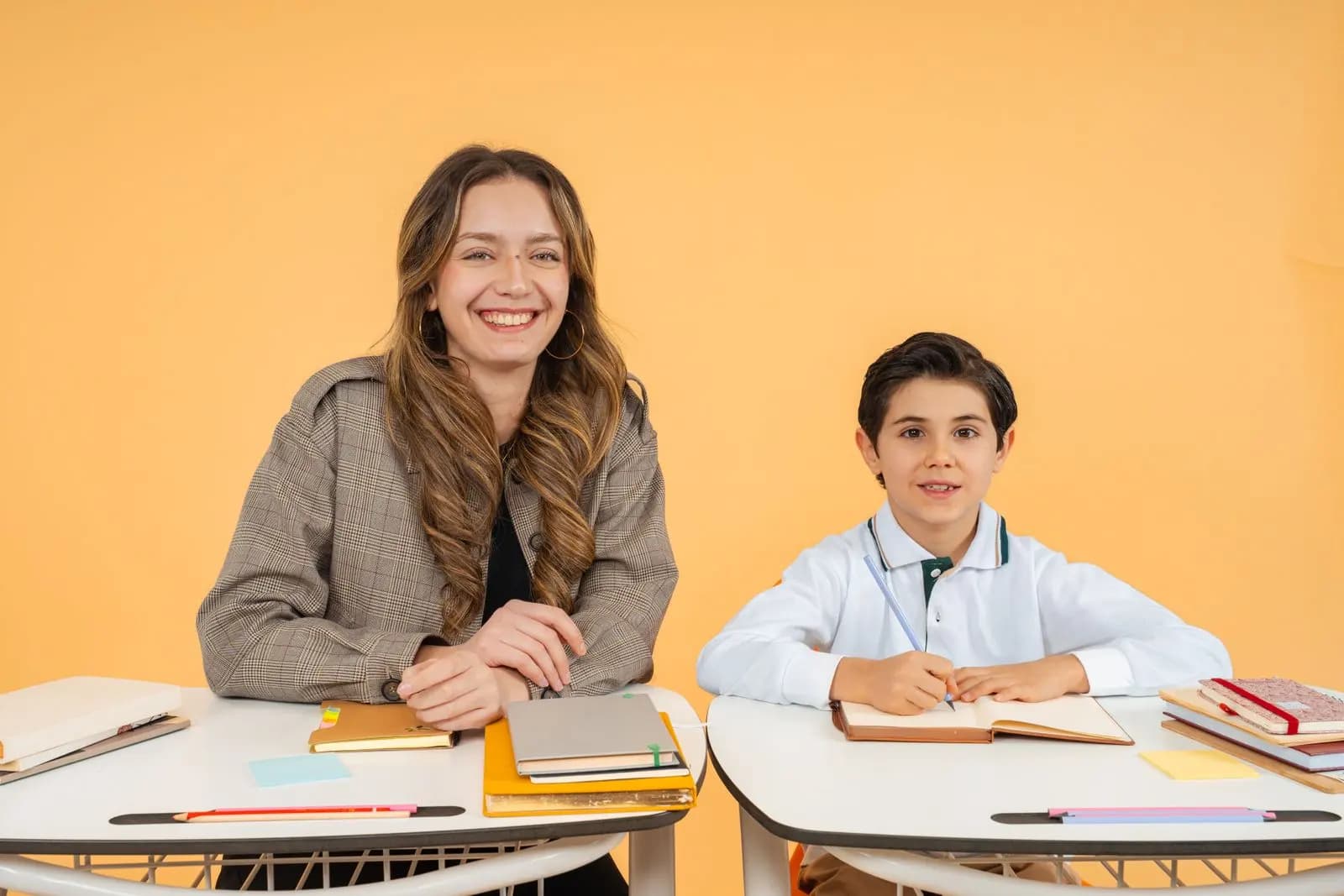 Professora e aluno sorrindo, sentados em mesas com livros e cadernos
