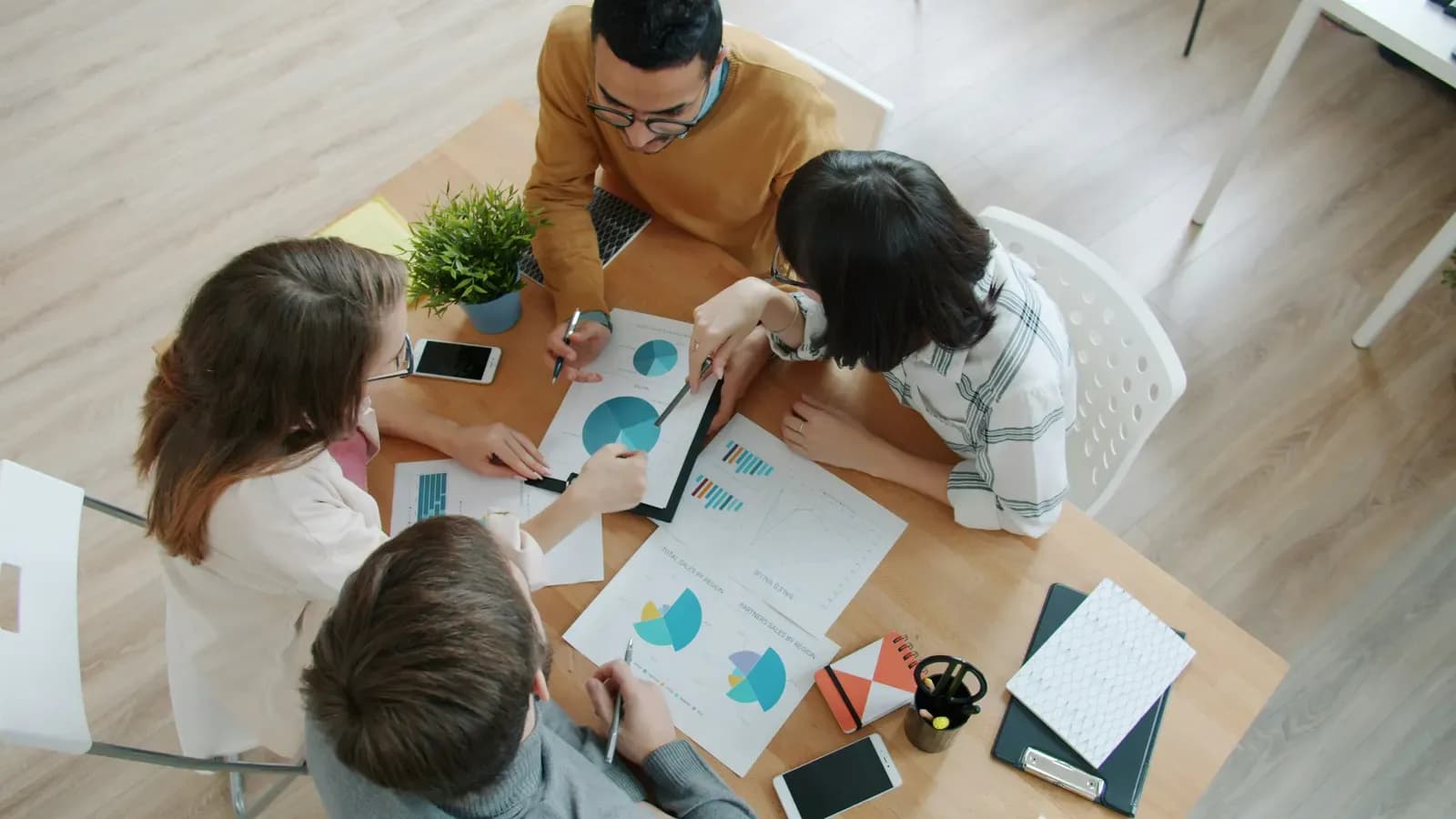 Quatro pessoas reunidas em volta de uma mesa, analisando gráficos impressos